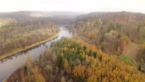 Done-flight-over-river-in-autumn-towards-a-single-bridge-decorated-with-Latvian-flags