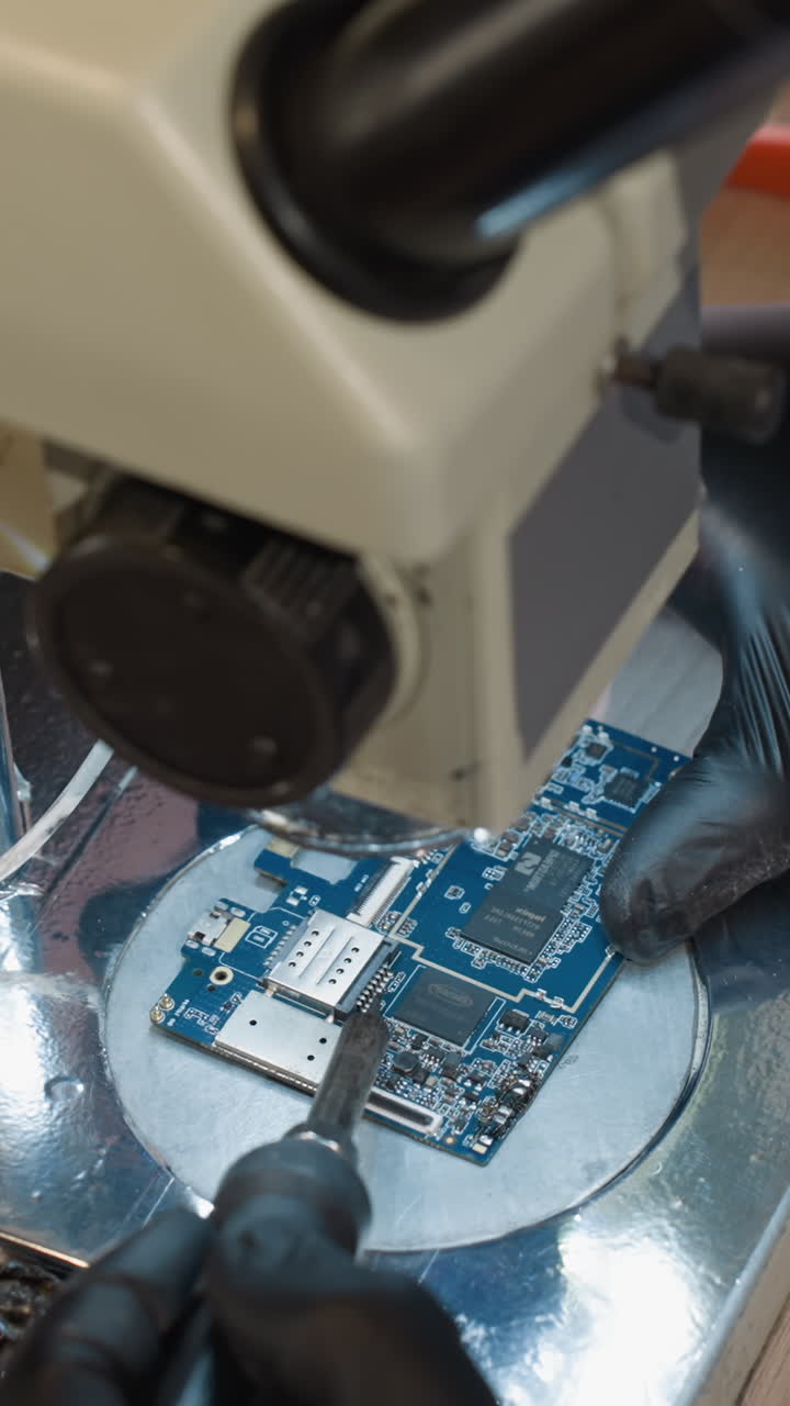 una vista de cerca de un técnico examinando una placa de circuito bajo un microscopio, el espacio de trabajo está equipado con varias herramientas y dispositivos