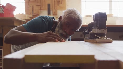 african american male carpenter blowing the dust over wooden plank at a carpentry shop