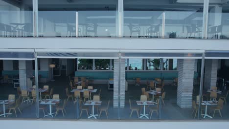 aerial footage gliding along the balcony of a tourist resort building, featuring a glass fence, along with chairs and tables