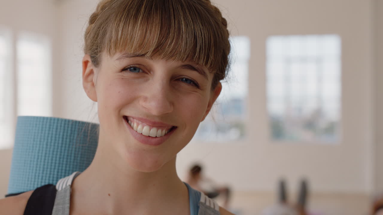 retrato hermosa mujer caucásica de yoga sonriendo con confianza disfrutando de un estilo de vida saludable con gente practicando en el fondo del gimnasio