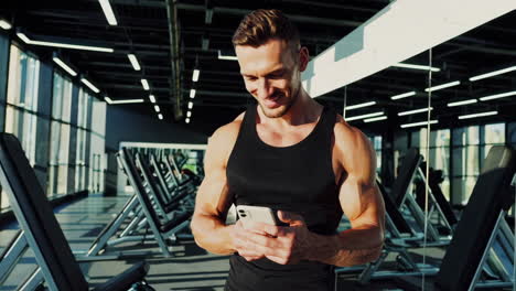 muscular man smiling and using smartphone in modern gym