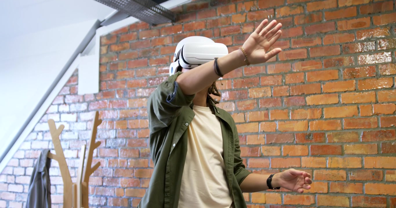 Homem afro-americano usando headset VR branco em loft, respondendo a comandos virtuais, gesticulando