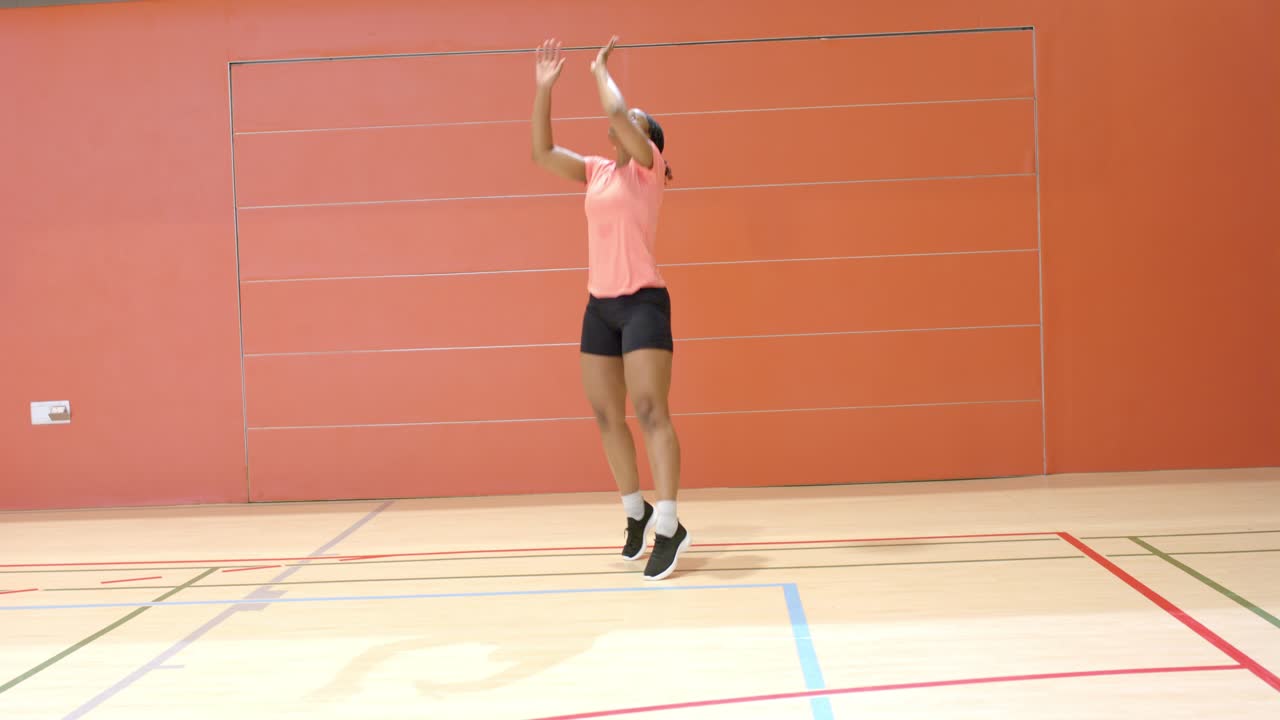 Donna afroamericana che si sposta contro una parete rossa della palestra, entra in campo e serve a pallavolo.