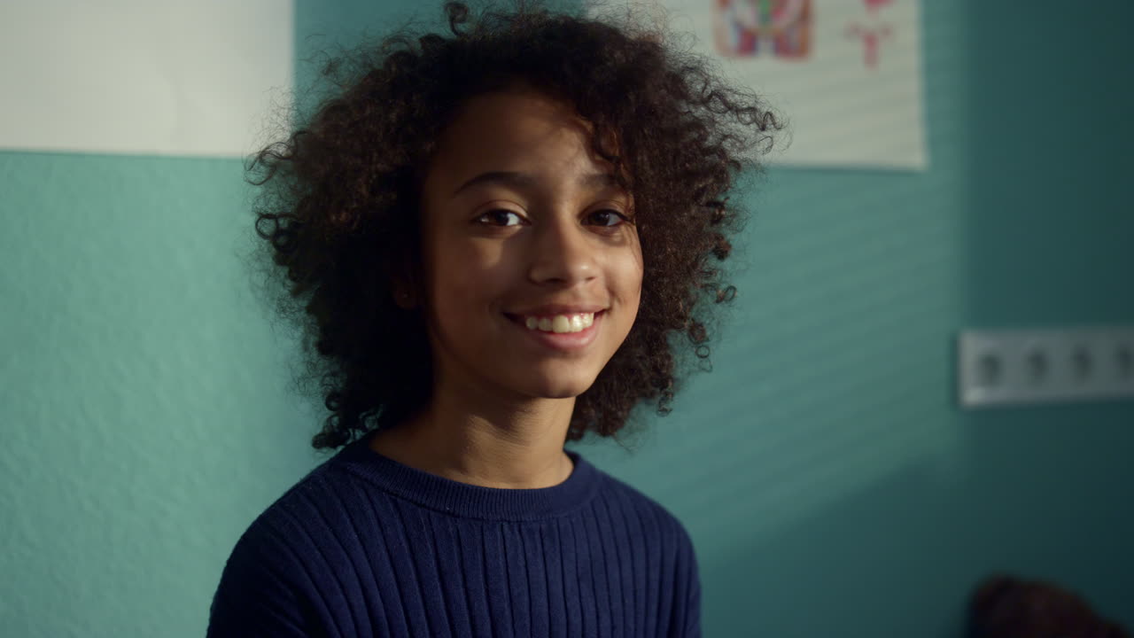 Portrait smiling african girl sitting modern clinic. Preteen kid visiting doctor