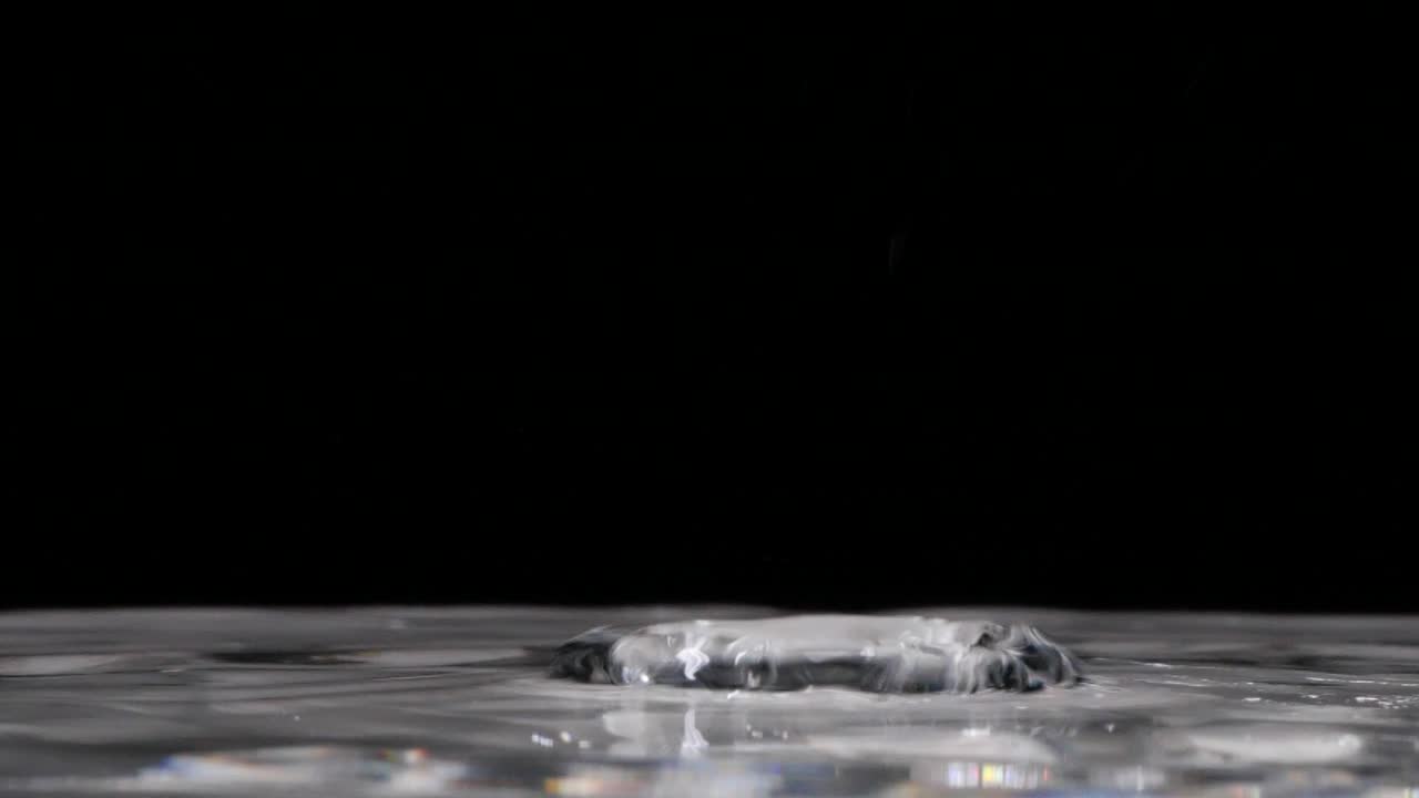 cierre extremo de las gotas de lluvia cayendo en una piscina de agua clara, cámara lenta