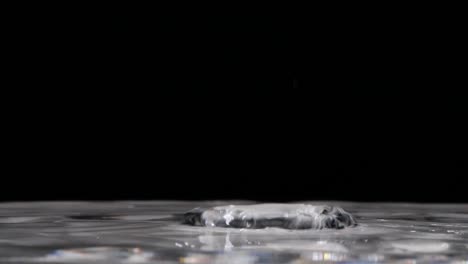 Extreme-closeup-of-raindrops-falling-into-clear-pool-of-water,-Slow-Motion