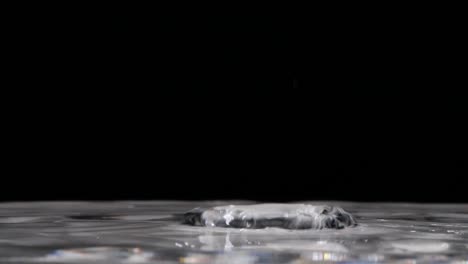 extreme closeup of raindrops falling into clear pool of water, slow motion