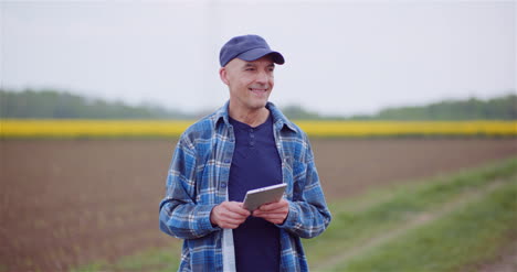 agricoltore che esamina il campo agricolo mentre lavora al computer tablet digitale presso l'azienda agricola 34