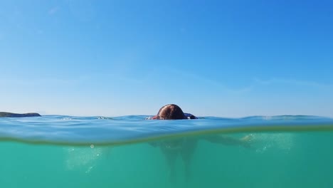 Young-red-hair-girl-swimming-undersea.-Half-underwater-view