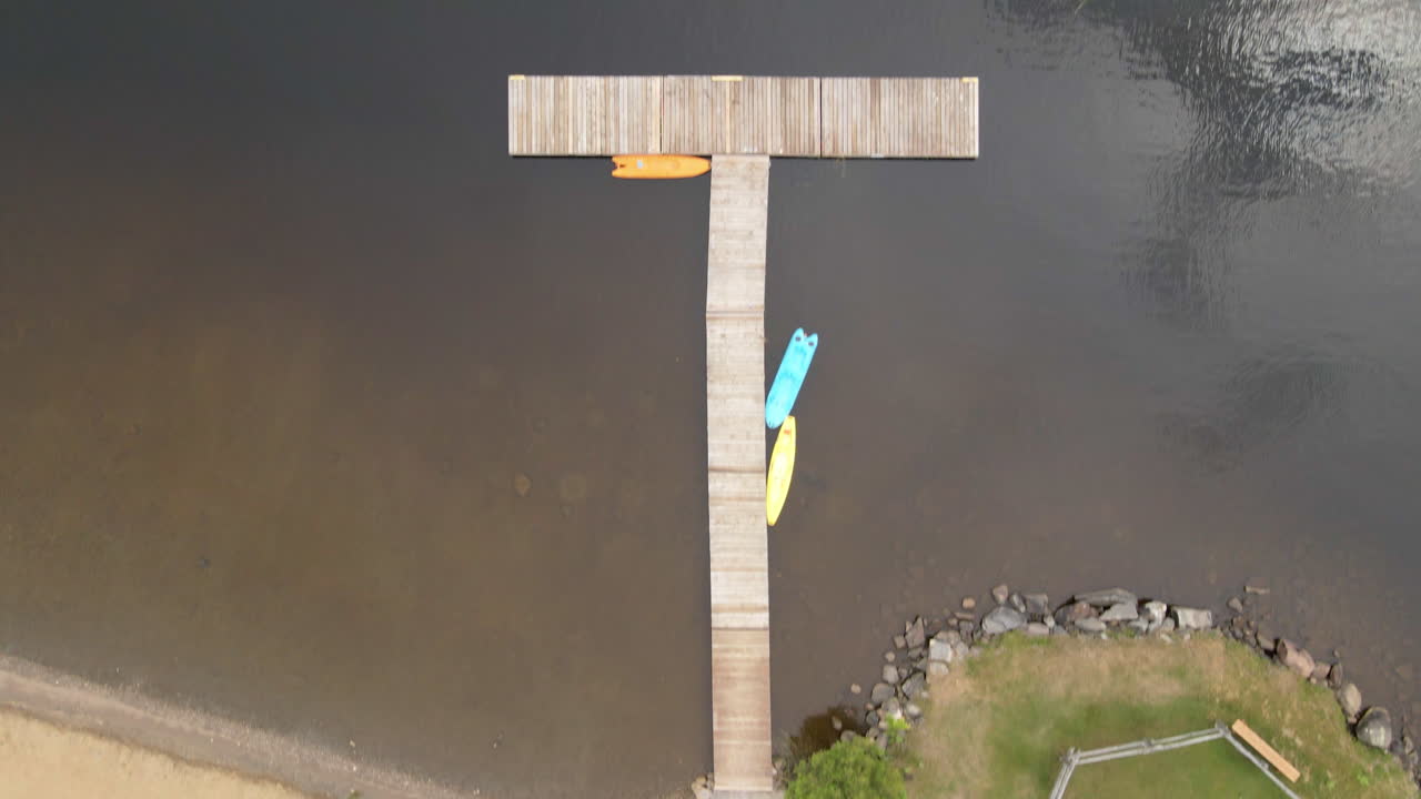 Aerial shot looking down over edge of beach with dock following into kayaks and paddleboards along the calm water. Calabogie Ontario