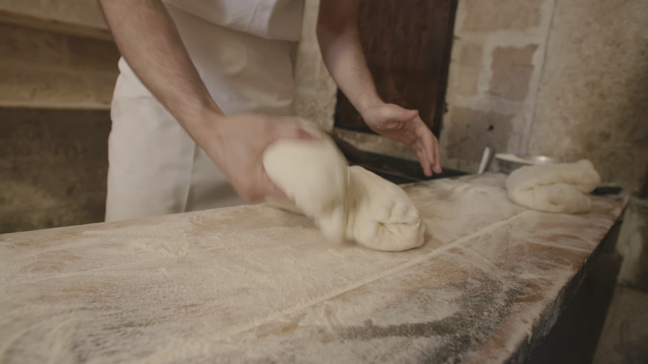 Un panettiere piega e impasta velocemente della pasta in una panetteria.