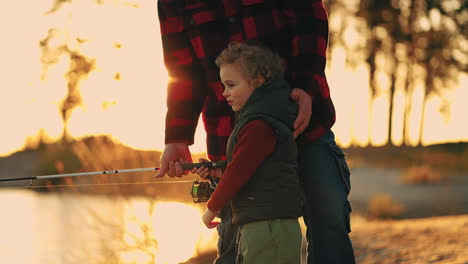 happy little boy with curly hair is fishing by rod granddad or father is helping child