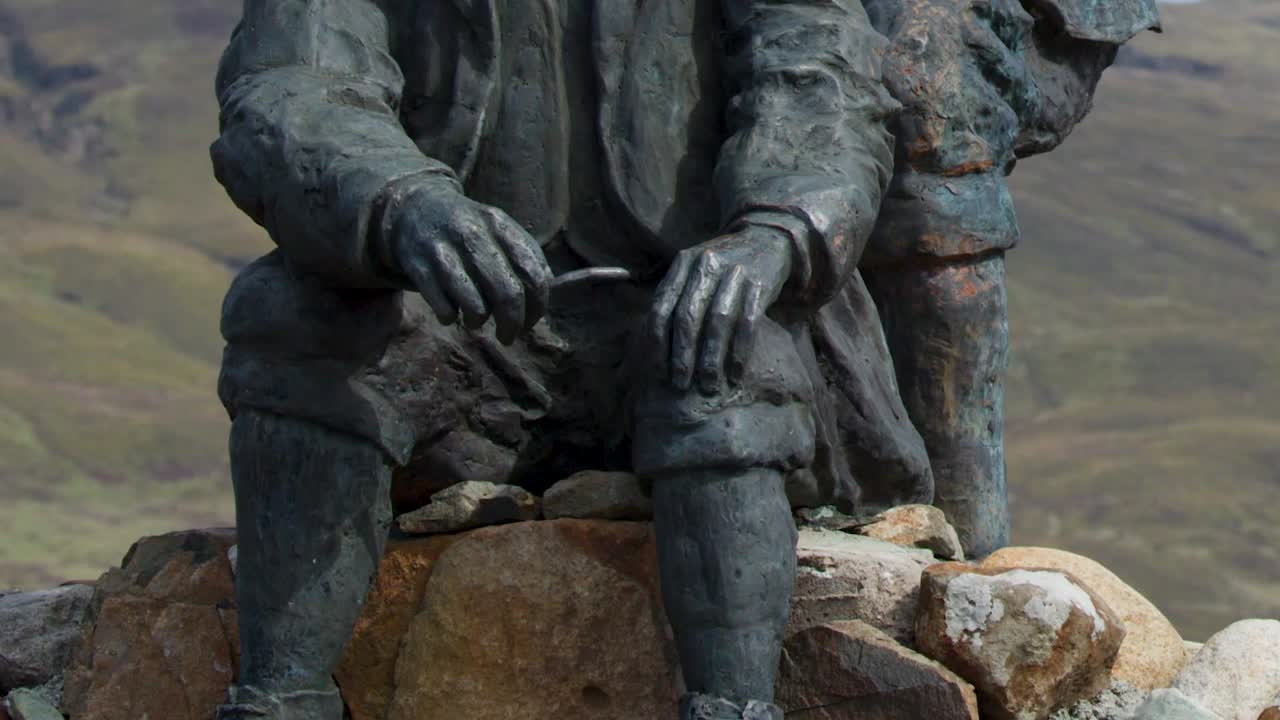 Eine detaillierte Nahaufnahme einer bronzenen Gedenkskulptur, die zwei Männer vor sanften Hügeln zeigt
