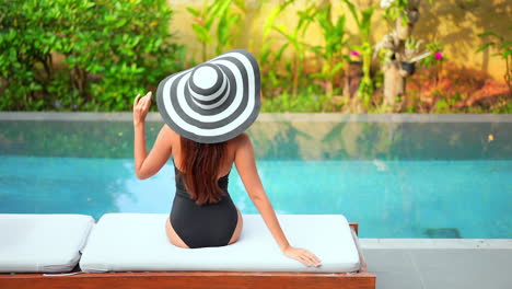 glamour female in swimsuit and big summer hat by pool on a tropical destination