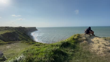 Tourist-sitting-on-top-of-cliff-taking-photos-of-mulberry-Harbour