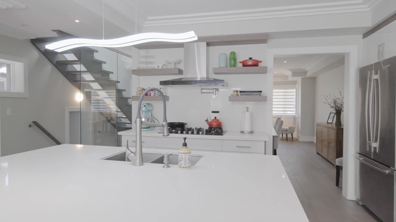 Mid range orbit shot of the kitchen counter and stove with the see through glass wall stairs at the left and a part of dinning room behind the kitchen in a house