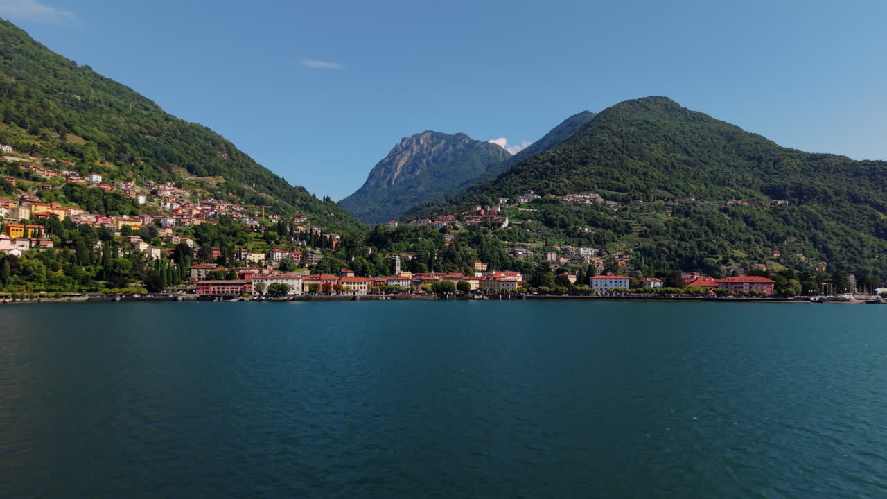 Drone flying forward over Lake Como toward a lakeside town with colorful buildings and mountains in the background