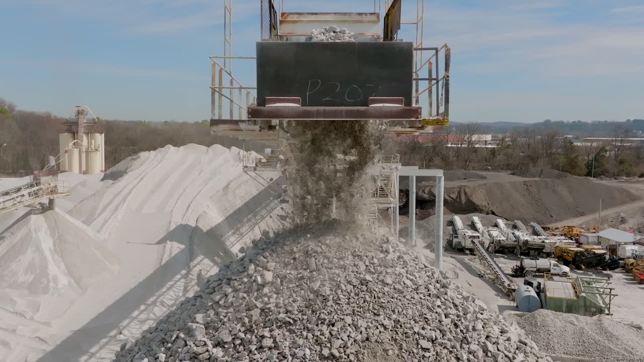 Static slow motion footage of gravel rocks being dropped off a conveyor belt and falling into a large pile.