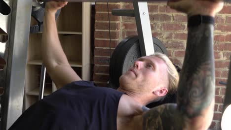 muscly man in home gym exercising smith machine barbell chest press