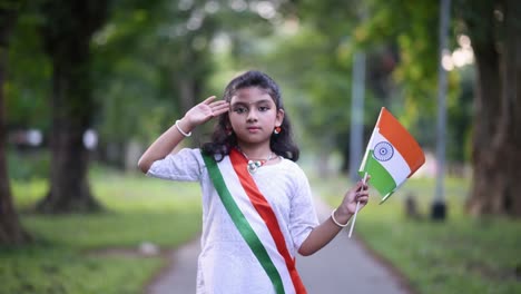 A-little-Indian-girl-is-celebrating-Indian-Independence-day-by-waving-a-tricolor-flag-of-India-and-salutes-in-outdoor-in-slow-motion