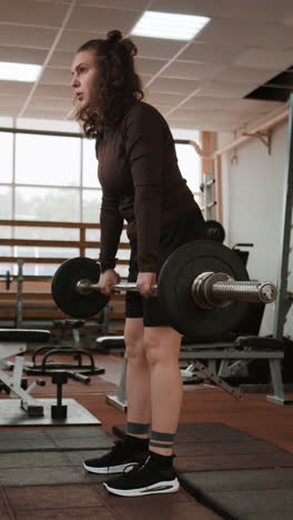 woman performing deadlifts with a barbell in a gym