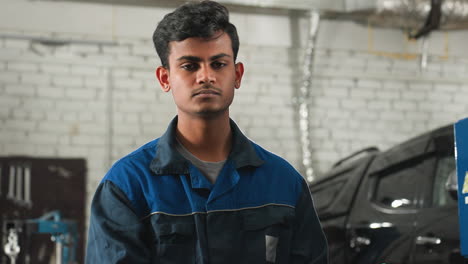 mecánico en uniforme azul inclinando la cabeza hacia la izquierda y la derecha con los ojos cerrados, mientras el colega mira a la cámara, la luz de fondo brillante crea un efecto de silueta en el taller de automóviles con el coche en el fondo
