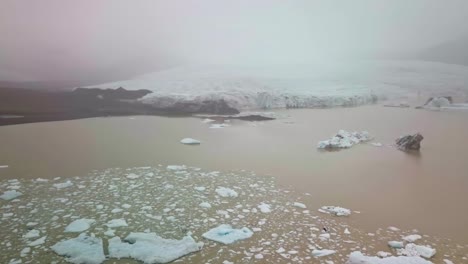 Muddy-lagoon-filled-with-icebergs-with-a-glacier-in-background