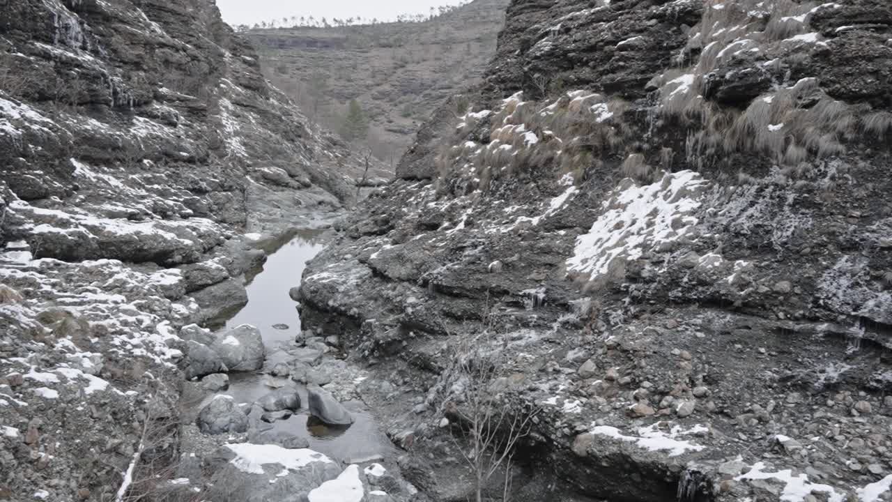 arroyo de invierno que fluye a través de un terreno rocoso con manchas de nieve, día nublado, luz natural