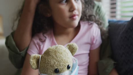 Mixed-race-mother-and-daughter-hugging,daughter-holding-tedy-bear-with-face-mask