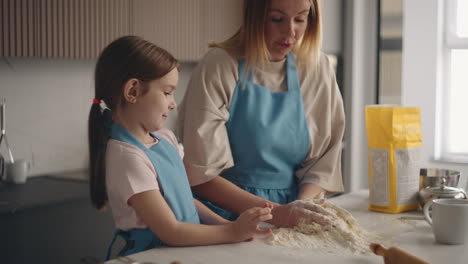 mother and child are making dough for cake or pie in home kitchen daughter is helping to mom