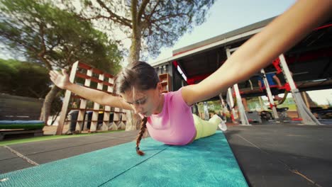 young woman doing back exercises on a mat at an outdoor gym