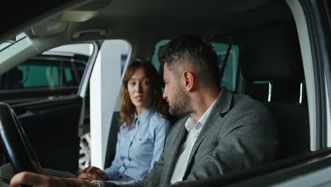 una pareja discutiendo un coche en una sala de exposiciones.