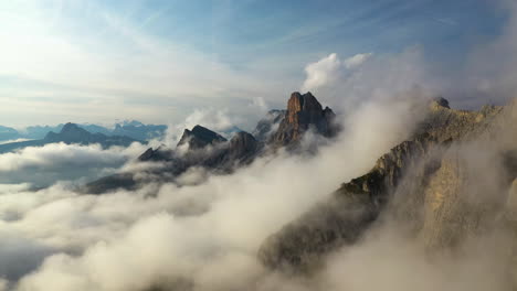 Aerial-view-flying-along-a-foggy-mountain-range,-sunny-day-in-Dolomites,-Italy