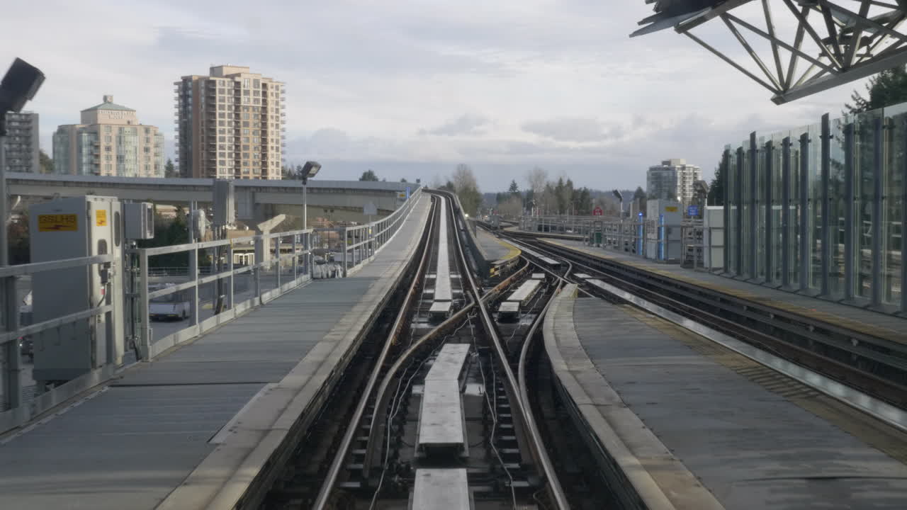 밝은 흰색 하늘 아래 높은 건물로 둘러싸인 고속도로 위의 밴쿠버 지하철에 있는 밀레니엄 라인 스카이 트레인 - 와이드 샷