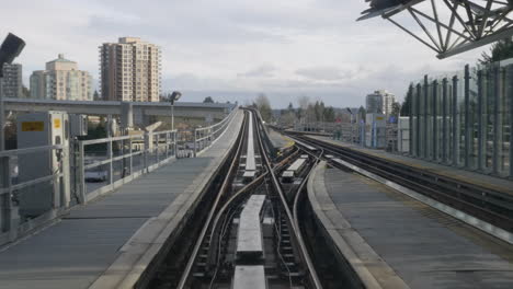 The-Millenium-Line-Sky-Train-In-Vancouver-Metro-Above-The-Highways-Surrounded-With-Tall-Buildings-Under-The-Bright-White-Sky---Wide-Shot