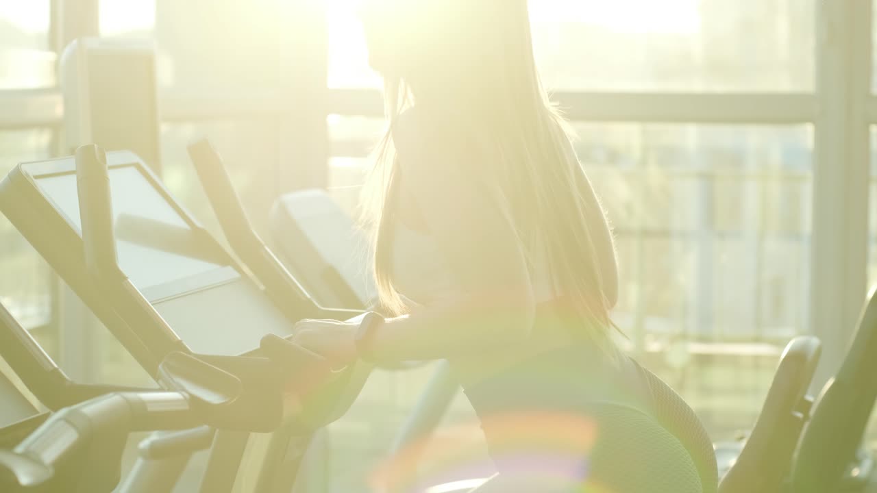 운동선수 여성은 체육관에서 오비트레크를 고 있습니다. 소녀는 심장 강도 및 내구성을 향상시키기 위해 스테퍼에서 운동하고 있습니다.