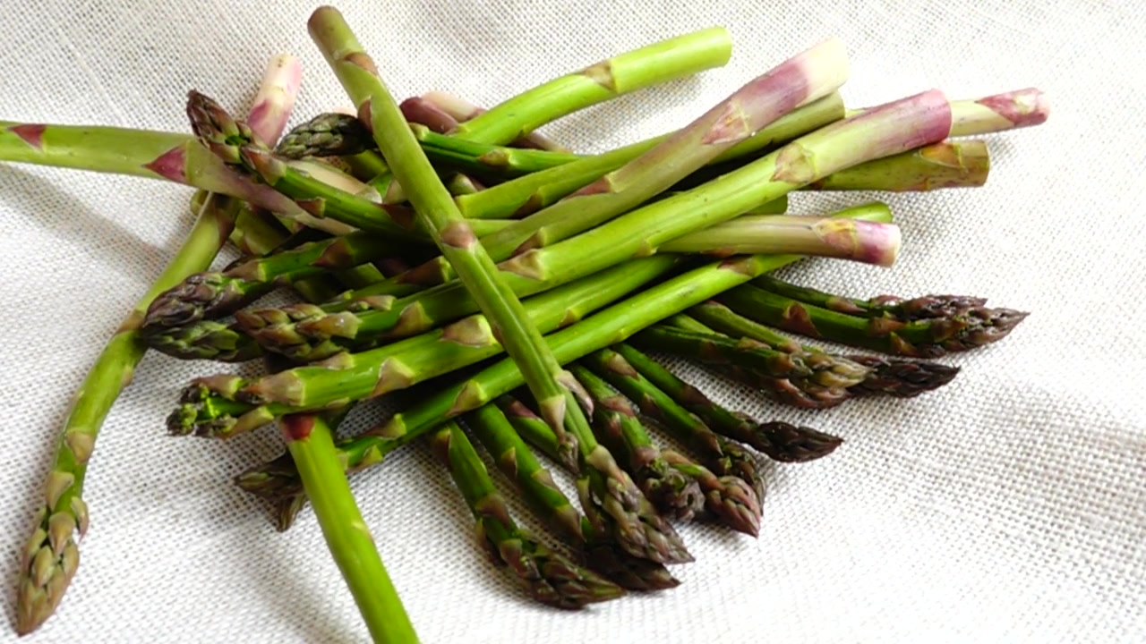 Fresh green asparagus falls on burlap. Slow motion.