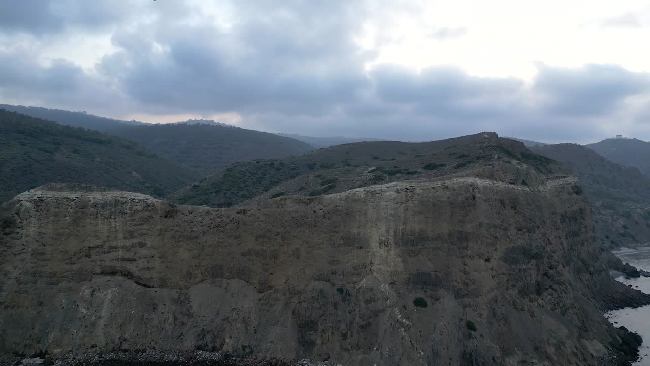 una vista impresionante se despliega mientras volamos por encima del mar mediterráneo, revelando un vasto acantilado, majestuosas montañas y bosques distantes en el fondo de un día nublado y grisáceo