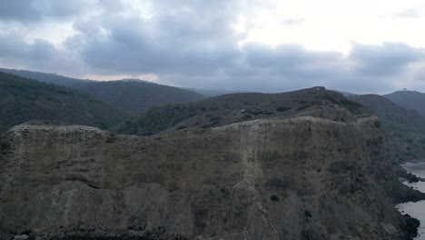 Una-Vista-Impresionante-Se-Desarrolla-Mientras-Nos-Elevamos-Sobre-El-Mar-Mediterráneo,-Revelando-Un-Vasto-Acantilado,-Majestuosas-Montañas-Y-Bosques-Distantes-En-El-Contexto-De-Un-Día-Nublado-Y-Grisáceo.