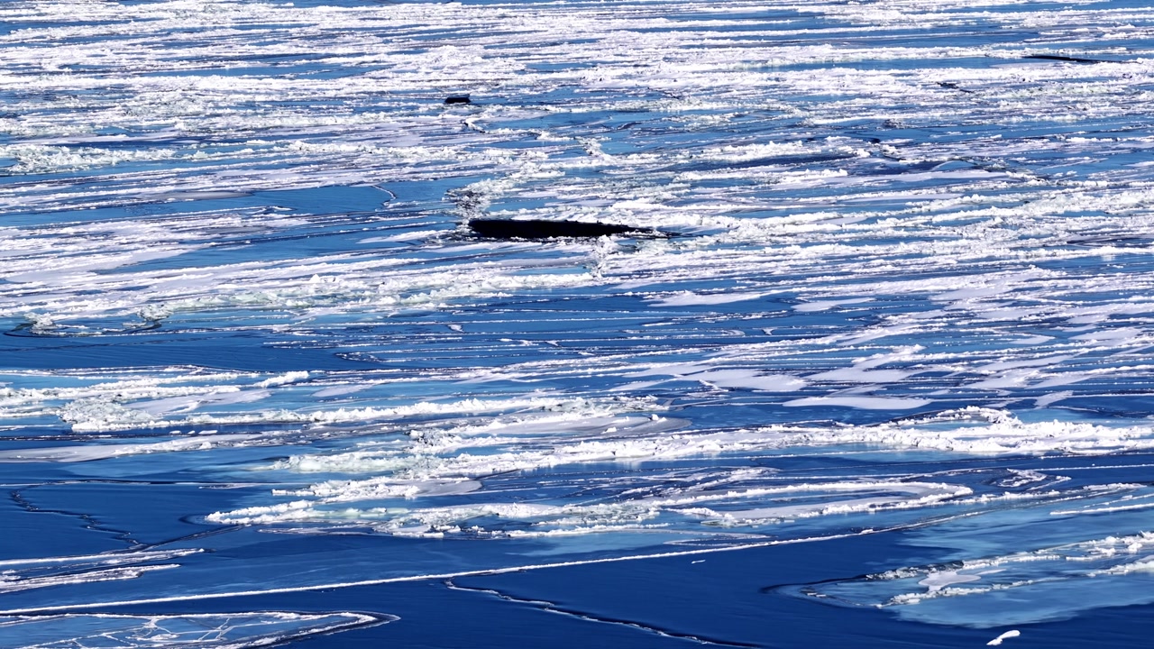 Drone shot glides above winter landscape featuring deep blue water and white ice floes on surface of frozen Riga gulf during cold season