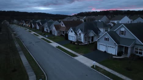 Vista-Crepuscular-De-Una-Calle-Suburbana-Con-Casas-De-Diseño-Uniforme,-árboles-Desnudos-Y-Un-Cielo-Crepuscular-Con-Tonos-Rosados