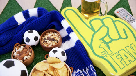 Bowl-of-snacks,-football,-beer,-foam-finger-and-shawl-on-artificial-grass-4k