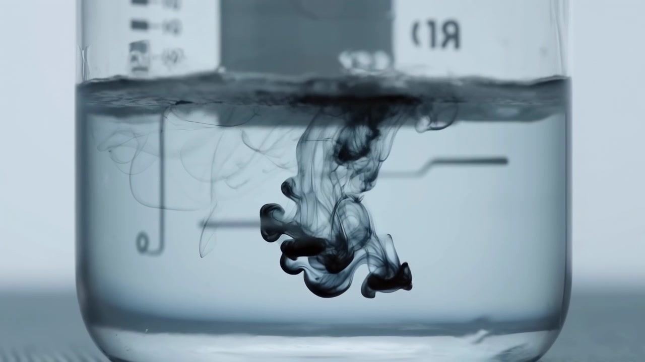Close view dark ink sinking and spreading in transparent beaker, forming soft plumes, swirls, and delicate gradients under cool laboratory light