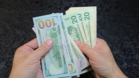 close-up of hands counting us banknotes on a table with a dark background