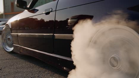 a black shiny car with tuning adjustments drifts in place and creates smoke from the tires