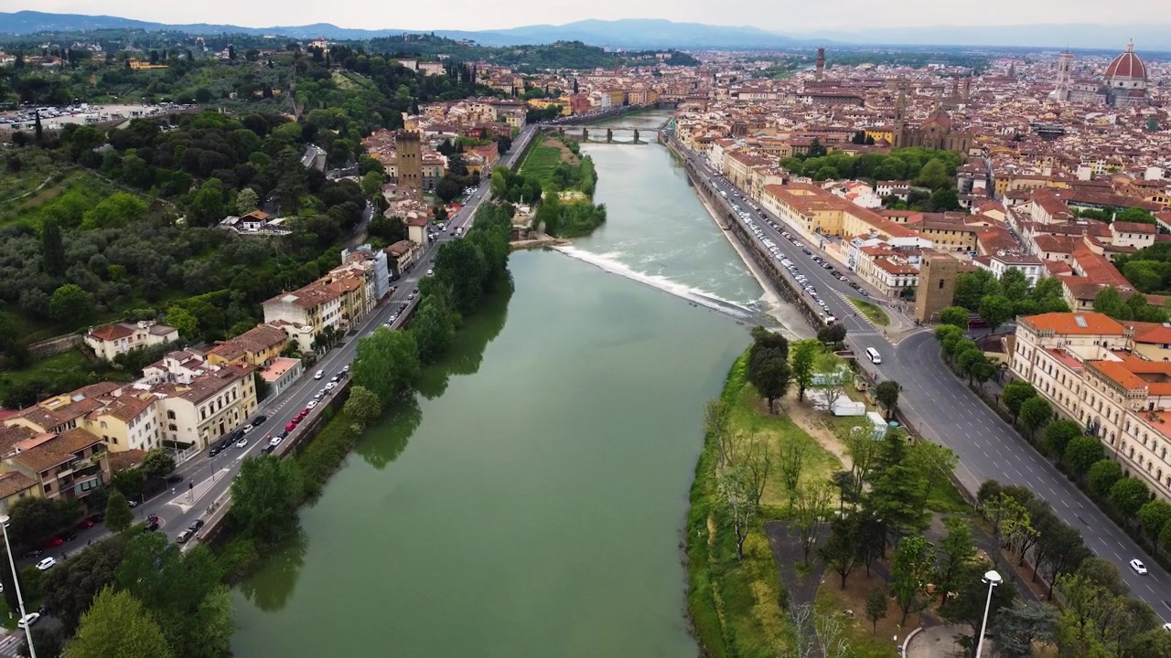 Toma aérea con dron a lo largo del río Arno a través de Florencia, Italia. Puentes históricos, terraplenes de la ciudad y la cúpula de la Catedral de Santa María del Fiore visibles en todo el horizonte