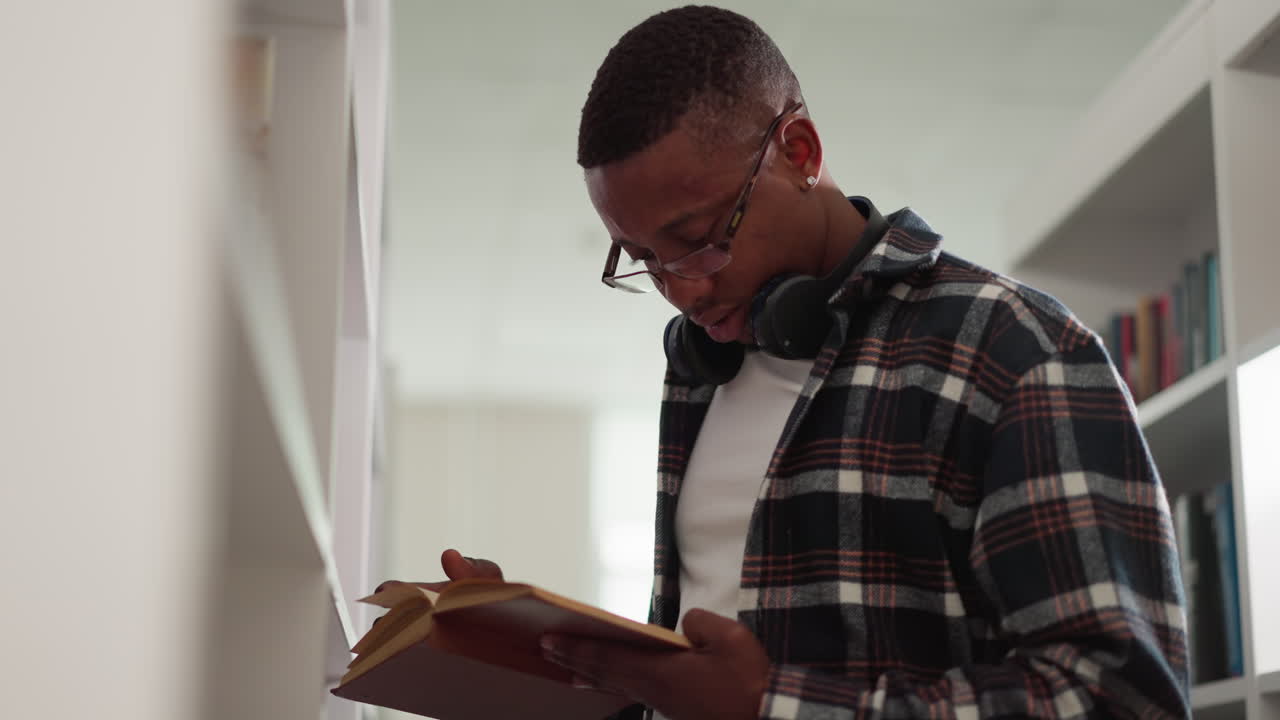 Guy reads book working in college library. African American man visits bookstore to get textbooks for education project. Rapt reader with favorite novel