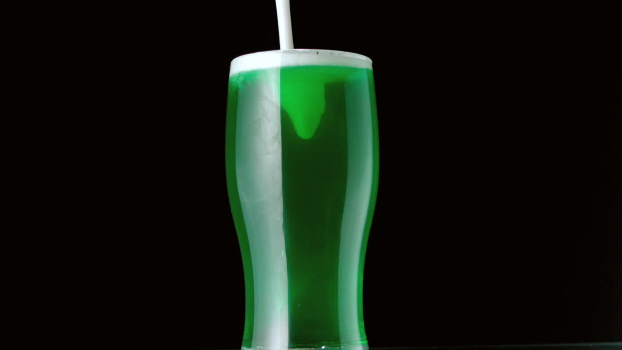 espuma vertiendo en una pinta de cerveza verde sobre un fondo negro