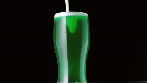 foam pouring onto pint of green beer on black background